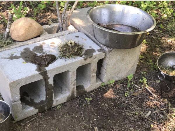 “Outdoor rustic mud kitchen diy made from cinder blocks, strewn with metal pots and pans.